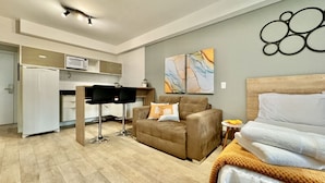 A compact living space with a kitchenette, a sofa, a bed, and a small table. - Studio Lindo, Condomínio Clube Lifespace Curitiba (Curitiba)