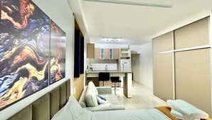 A modern hotel room with a sofa, a dining area, and a kitchen.