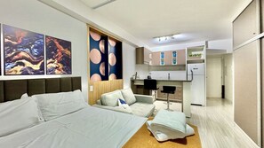 Una habitación de hotel moderna con cama, sofá, kitchenette y obras de arte en las paredes.