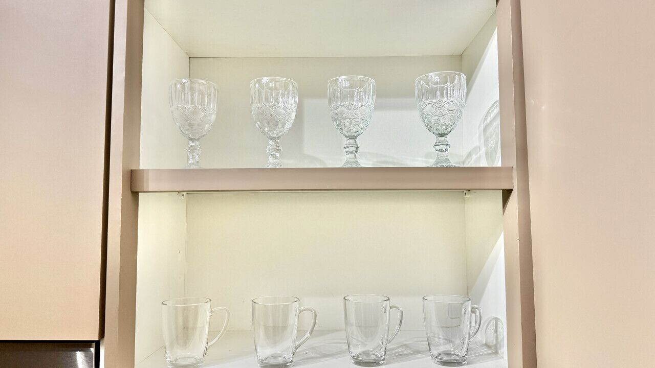 A shelf with three glass goblets and four clear glass mugs.