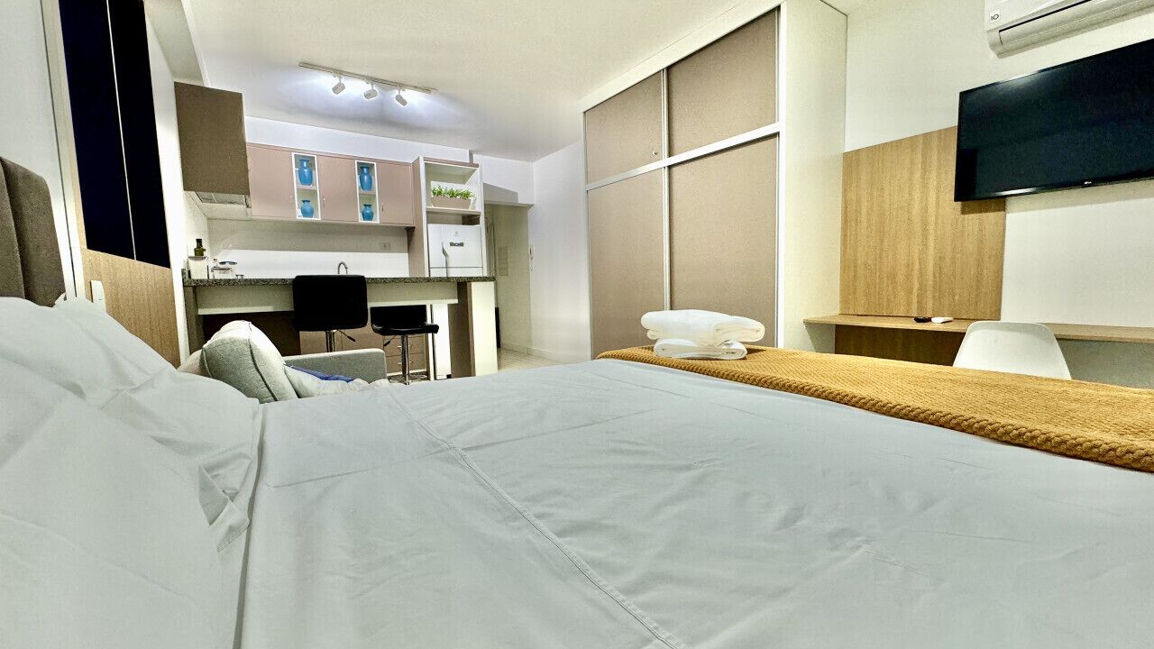 Ein Hotelzimmer mit Bett, Schreibtisch, Stuhl, Fernseher und einer Küchenzeile.