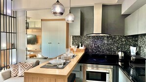 A modern kitchen with a central island, stainless steel appliances, and a dark tiled backsplash.