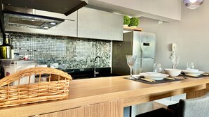A modern kitchen with a wooden countertop, a woven basket, and a dining area with white plates and glasses.