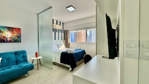 A modern hotel room with a bed, a small table, a blue sofa, and a painting on the wall.