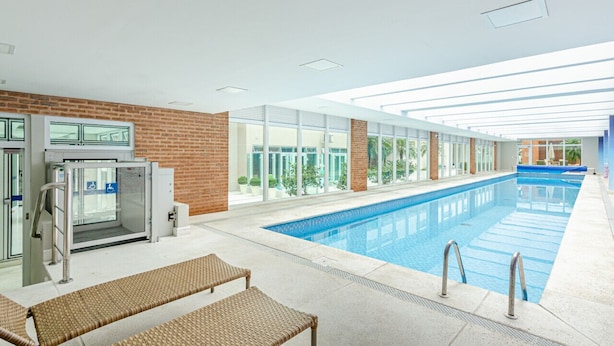 An indoor swimming pool with clear glass walls, a brick wall, and a glass door entrance.