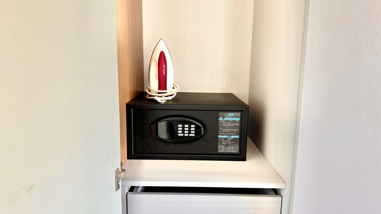 A microwave with a digital display and a remote control on a shelf.