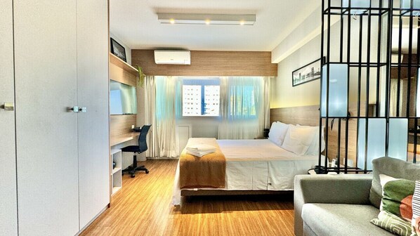 A modern hotel room with a bed, a desk, and a chair. There is a window with curtains and a view of the outside.
