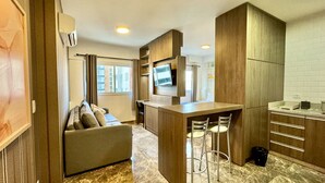 A compact hotel room with a kitchenette, a sofa, a TV, and a small dining area.