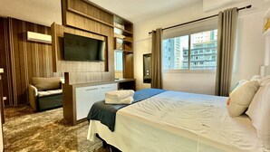 A hotel room with a bed, a TV mounted on the wall, a desk, and a window with curtains.