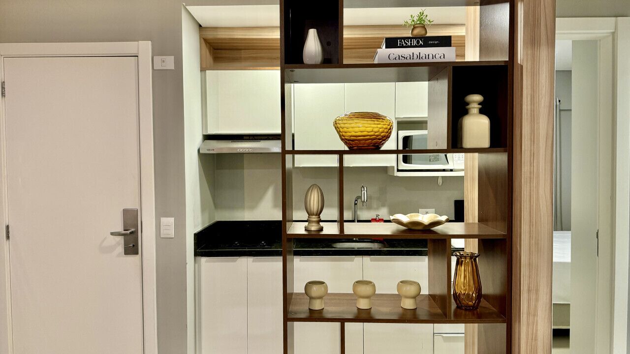 A kitchen with white cabinets, a microwave, and a wooden shelf with decorative items.
