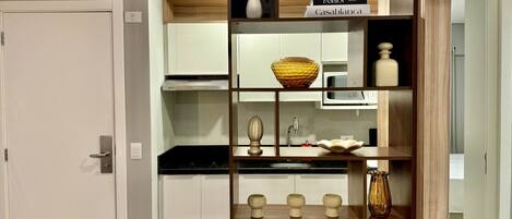 A kitchen with white cabinets, a microwave, and a wooden shelf with decorative items.