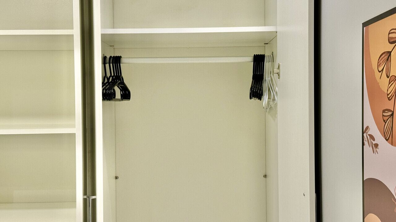 A hotel room with a white wardrobe, a bed, and a framed picture on the wall.