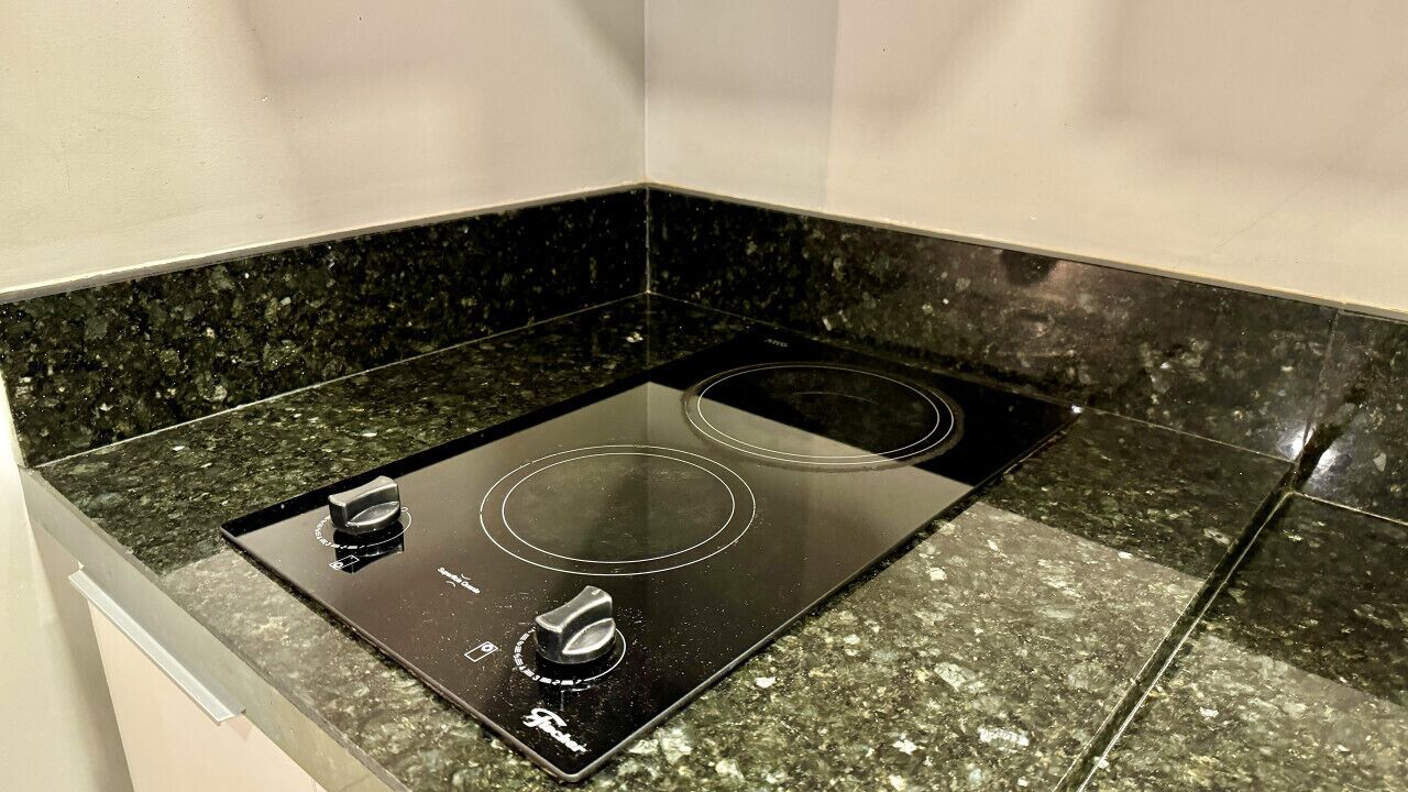 Una placa de inducción negra con dos mandos y una pantalla digital, sobre una encimera de granito.