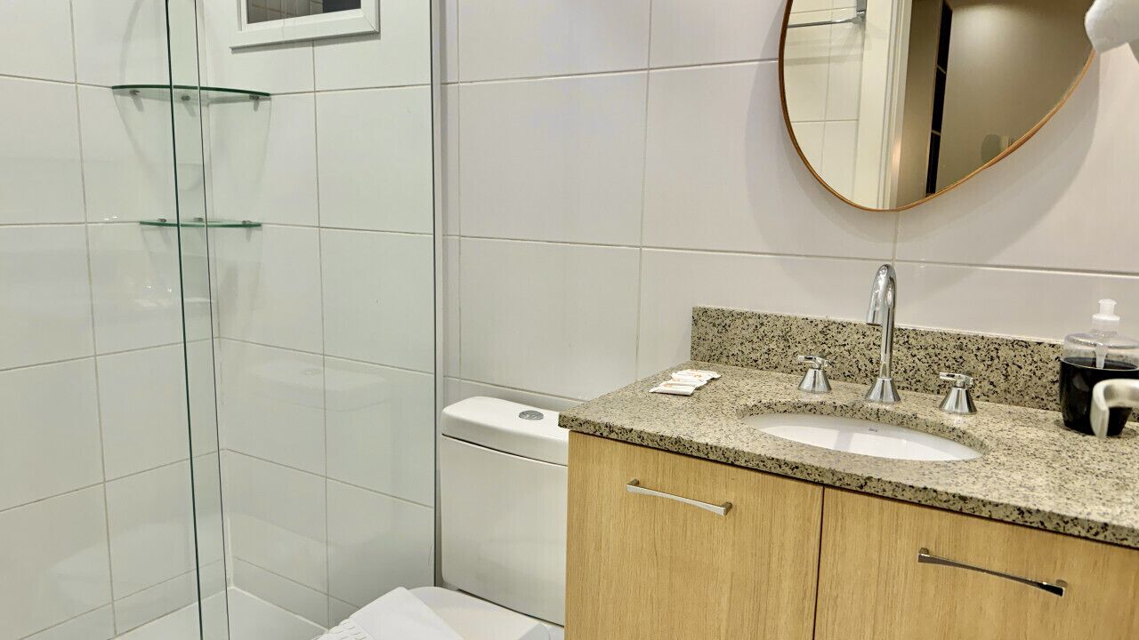 A modern bathroom with a glass shower enclosure, a granite countertop sink, and a round mirror.