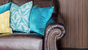 A brown leather sofa with four patterned cushions against a wooden panel wall.