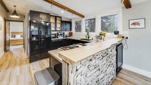 A modern kitchen with a large island, built-in appliances, and a stone accent wall. - 30-Day Pet Friendly, BBQ Grill, Walking Distance to Downtown and City Beach! (Whitefish)