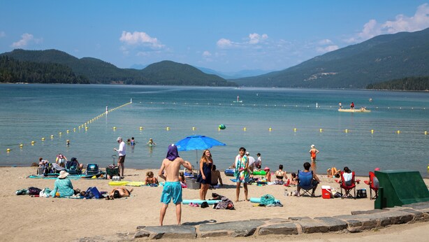A beach with people sunbathing, swimming, and using beach chairs. - 30-Day Pet Friendly, BBQ Grill, Walking Distance to Downtown and City Beach! (Whitefish)