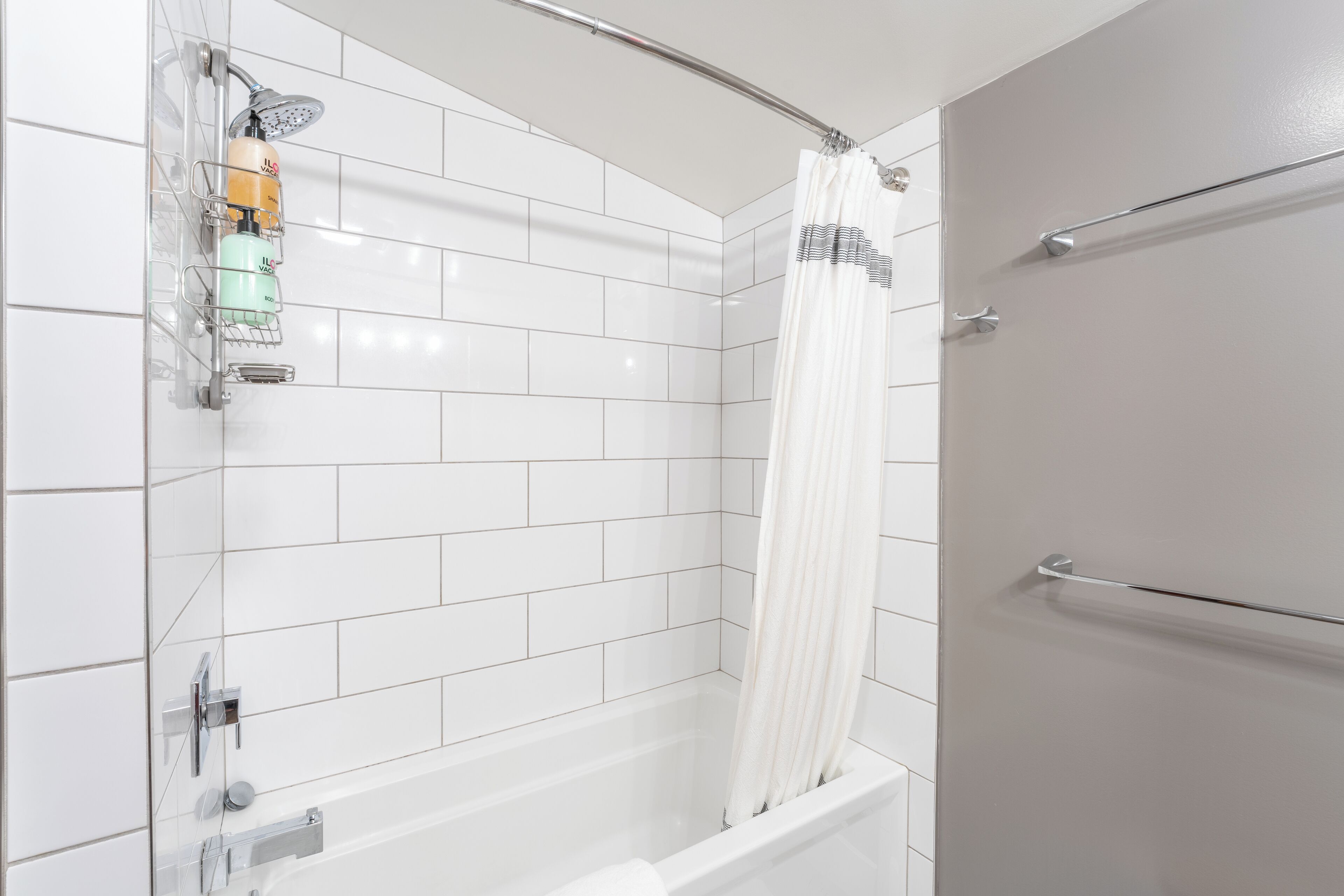 A modern bathroom with white tiled walls, a bathtub, a shower with a curtain, and a towel rack.