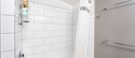 A modern bathroom with white tiled walls, a bathtub, a shower with a curtain, and a towel rack.