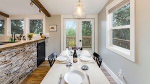 A dining area with a stone wall, a wooden table set for six, and large windows offering a view of the outdoors. - 30-Day Pet Friendly, BBQ Grill, Walking Distance to Downtown and City Beach! (Whitefish)