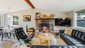 A modern living room with a stone fireplace, leather furniture, and a dining area with a wooden table and chairs. - 30-Day Pet Friendly, BBQ Grill, Walking Distance to Downtown and City Beach! (Whitefish)