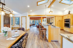 Una cocina amplia con armarios de madera, una isla central con taburetes de bar y un comedor con mesa dispuesta para cuatro.