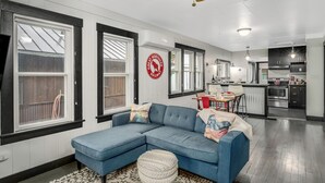 A modern living room with a sectional sofa, a dining area, and a kitchen with dark cabinets and stainless steel appliances. - 30-Day Min, Walking Distance to Downtown & Lake + Nearby Whitefish Mountain Resort! (Whitefish)