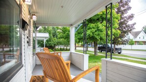 A covered porch with wooden chairs and a bench, overlooking a street with houses and a parked truck. - 30-Day Min, Walking Distance to Downtown & Lake + Nearby Whitefish Mountain Resort! (Whitefish)