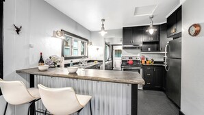A modern kitchen with a central island, bar stools, dark cabinetry, and a clock on the wall. - 30-Day Min, Walking Distance to Downtown & Lake + Nearby Whitefish Mountain Resort! (Whitefish)
