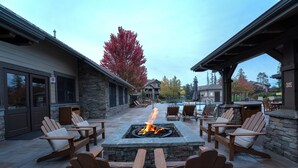 An outdoor patio with a stone fire pit surrounded by wooden Adirondack chairs and a stone table.