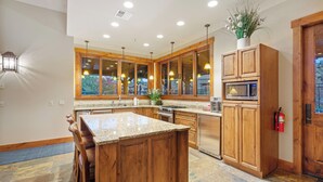 A modern kitchen with wooden cabinets, a granite island, and stainless steel appliances.