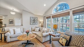 A spacious living room with a large window, a round coffee table, and two sofas. - 30-Day Min, Close to Downtown, Walk to Golf & Lake! (Whitefish)