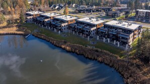 A modern residential complex with multiple apartment buildings, a small lake, and a mountainous backdrop. - Hot Tub + Close to Downtown, Smith Fields and Whitefish Mountain Resort! (Whitefish)