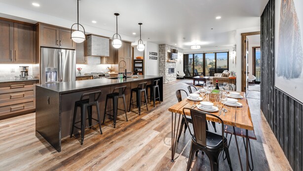 A modern kitchen with a central island, bar stools, and a dining area with a wooden table set for six. - Hot Tub + Close to Downtown, Smith Fields and Whitefish Mountain Resort! (Whitefish)