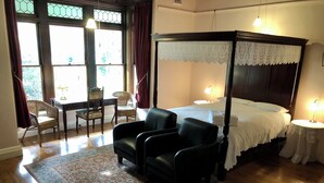 Une chambre à coucher avec un lit à baldaquin, deux chaises, une petite table et une table de chevet avec une lampe.
