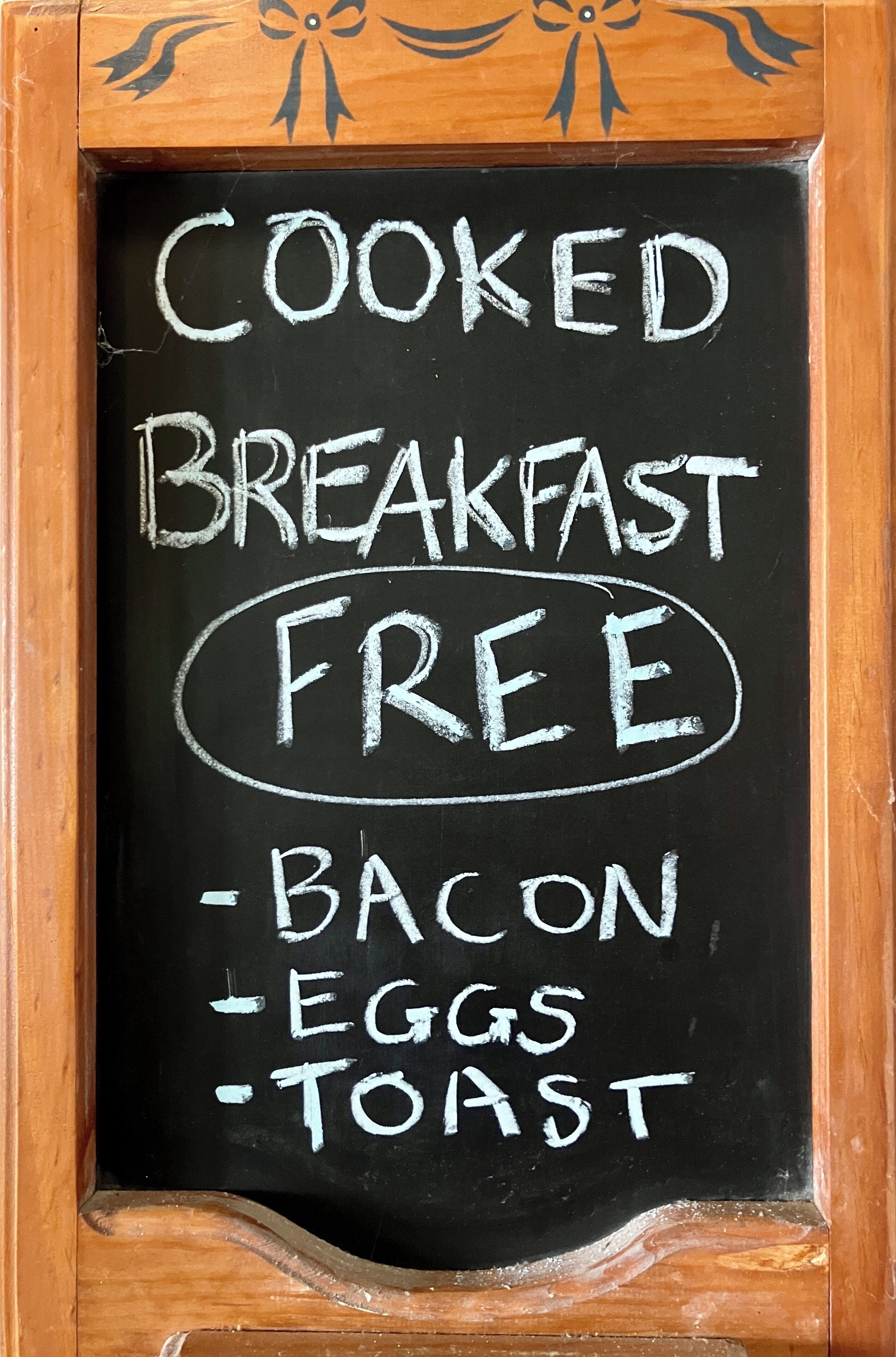 A blackboard with the text "COOKED BREAKFAST FREE - BACON - EGGS - TOAST".