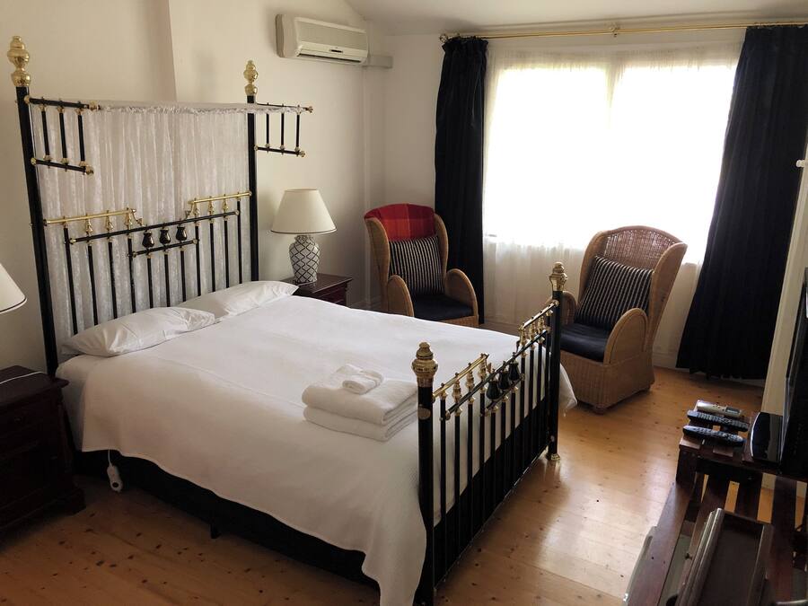 Una habitación de hotel con una cama grande, una mesita de noche con lámpara, una silla y una pequeña mesa con un control remoto.