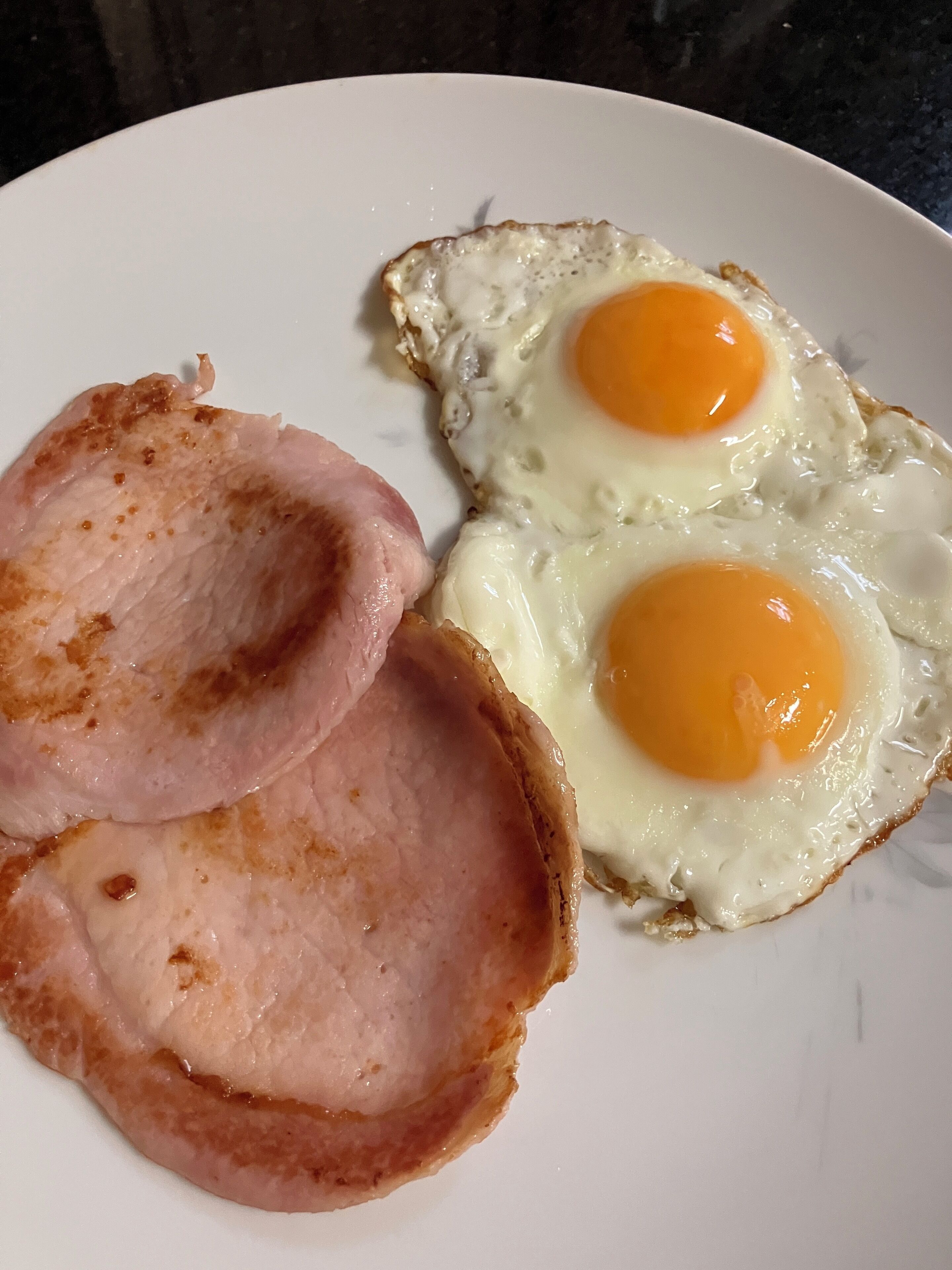 A plate with two fried eggs and two slices of ham.