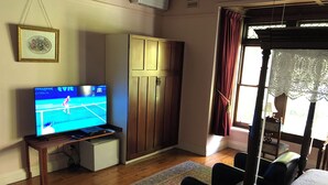 Une pièce comprenant un téléviseur diffusant un match de tennis, une armoire, un lit et une fenêtre avec des rideaux.