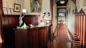 Un espace d’accueil avec un comptoir en bois, une statue, des tableaux encadrés et un tapis rouge menant à un escalier.
