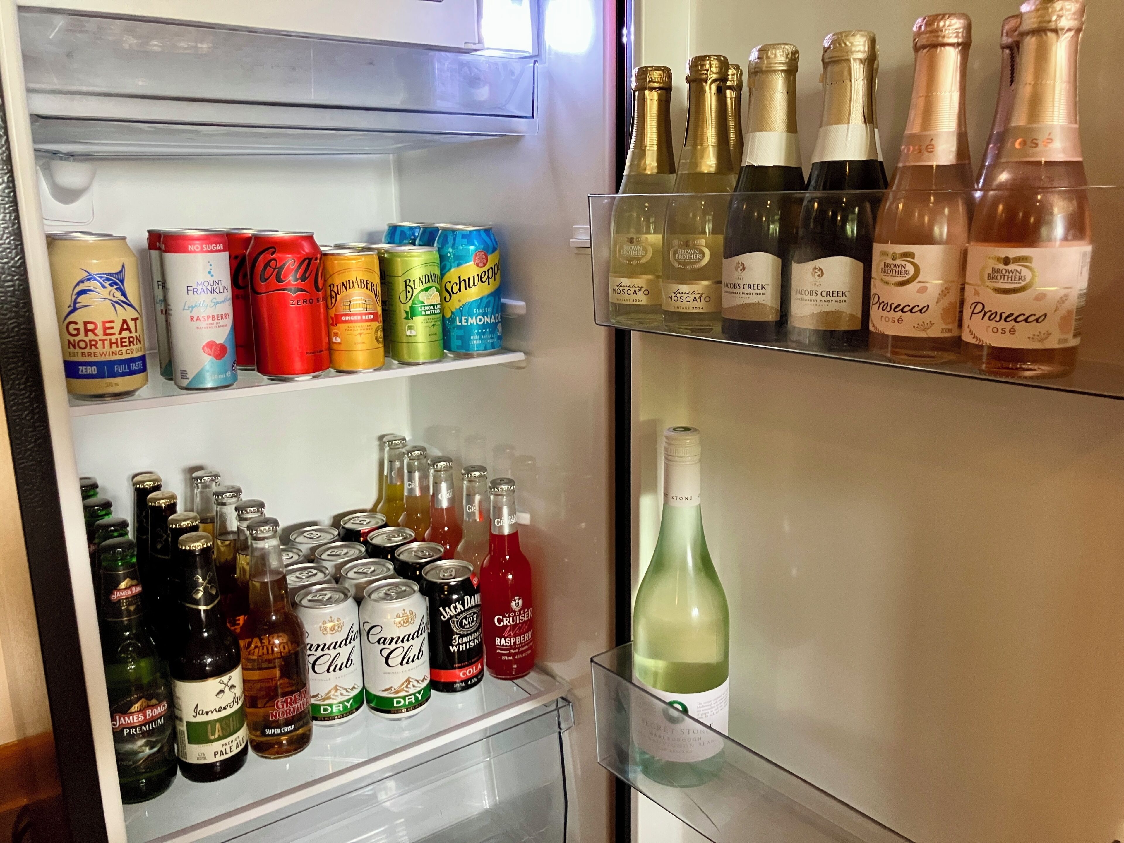 Un refrigerador lleno de diversas bebidas, incluyendo latas, botellas y vino.