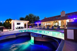 A swimming pool area with a hot tub, lounge chairs, and a covered seating area.
