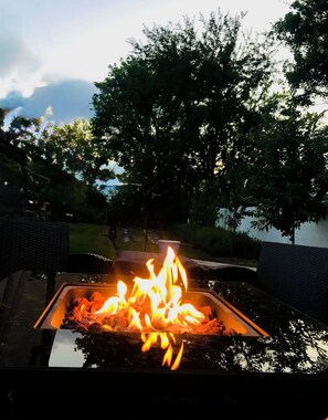 A rectangular outdoor fire feature with flames, surrounded by a grassy area and trees. - Luxurious 1875 Home, King Suite + Central Location (Uniontown)