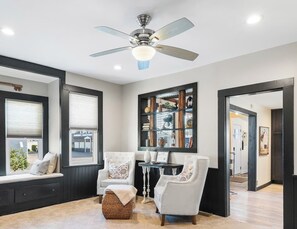 Un salon doté d’un ventilateur de plafond, d’une cheminée et offrant une vue sur l’extérieur grâce à de grandes fenêtres.