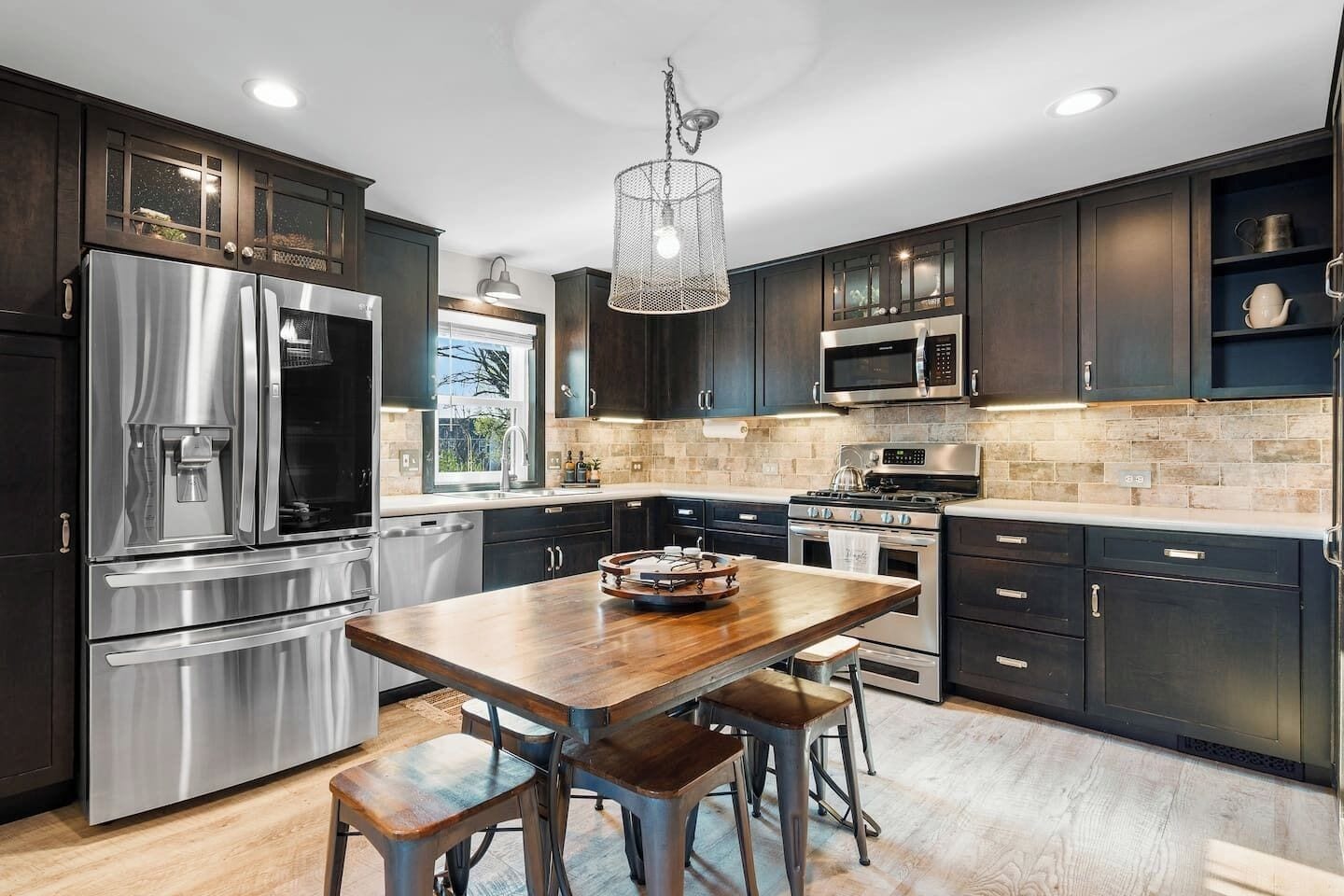 A modern kitchen with stainless steel appliances, dark cabinetry, and a wooden island with stools.