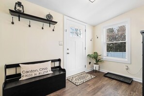 Un hall d’entrée propre et moderne, avec un banc, une plante en pot, un tapis et une porte dotée d’une fenêtre.