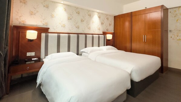 Una habitación de hotel con dos camas, un armario de madera y una mesita de noche con lámpara.