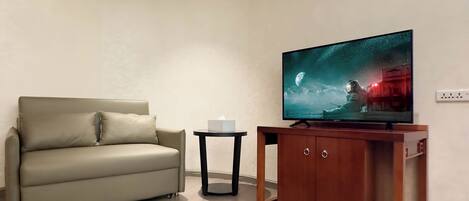 A living room with a sofa, a small side table, a television, and a wooden cabinet.