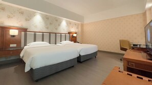 A hotel room with two beds, a desk, a chair, and a television.