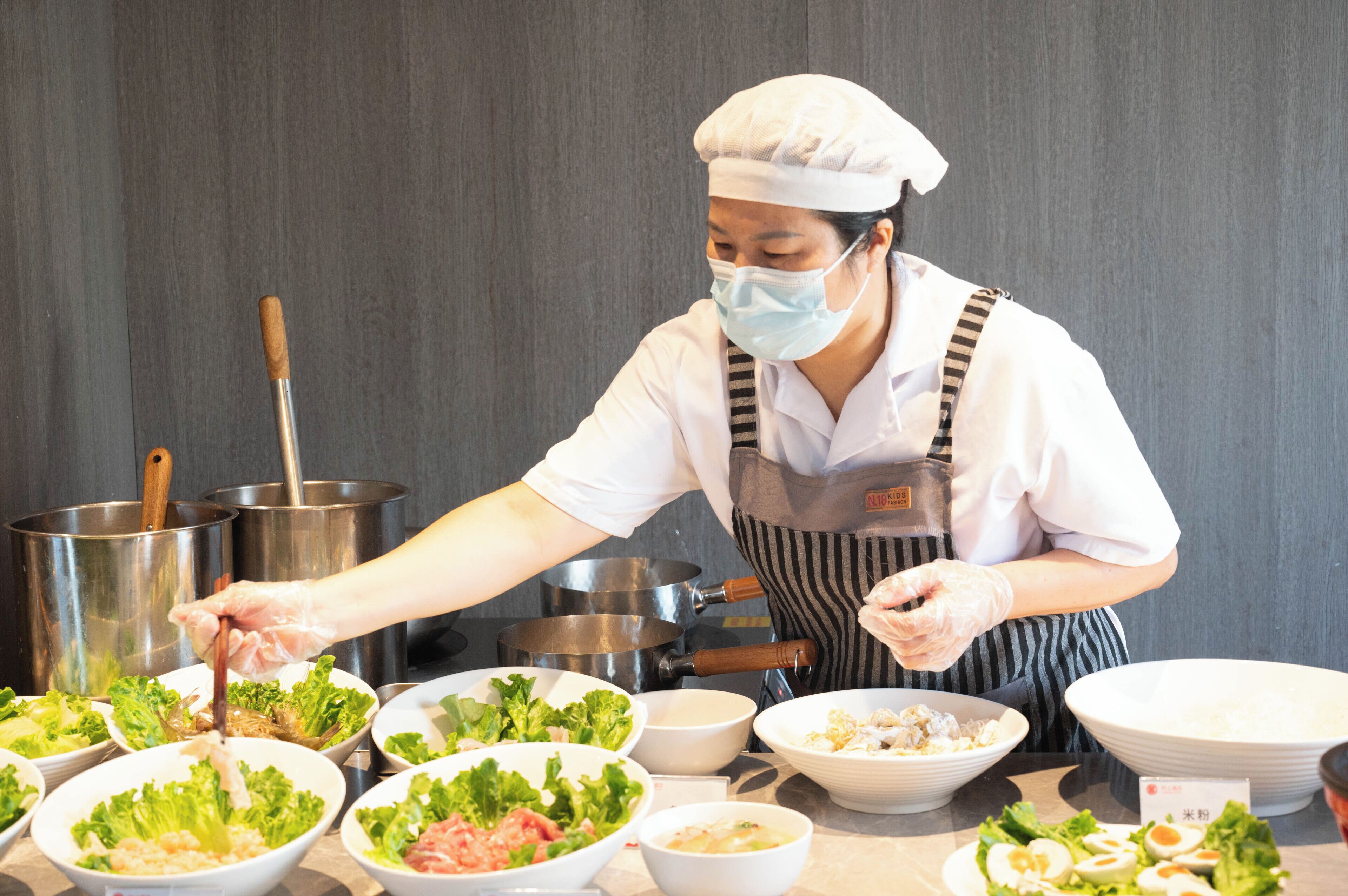 A chef preparing food in a kitchen with stainless steel pots and bowls of ingredients.